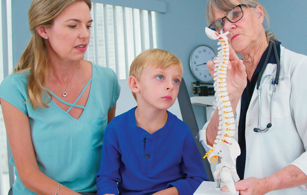 doctor showing spine model to a mother and her son